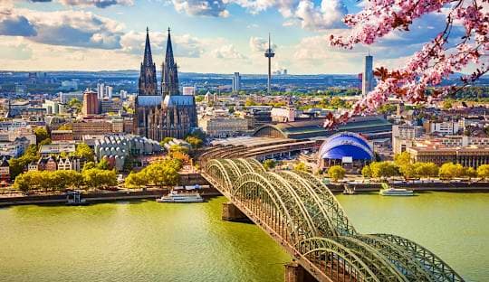 From Prague to Paris Cologne Cathedral and Hohenzollern Bridge spanning the Rhine River with spring blossoms in foreground